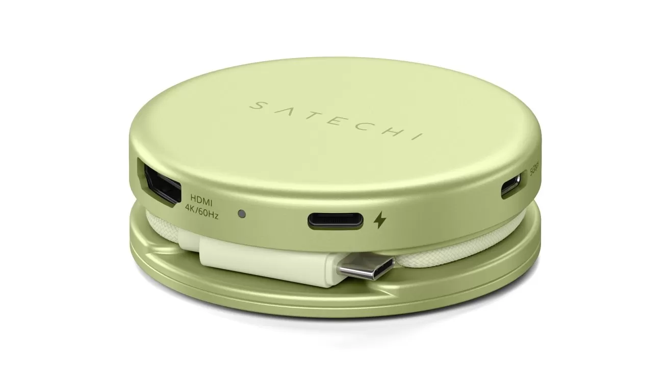 Round light-green Satechi portable USB-C hub with HDMI, USB-C, and other ports, cable wrapped neatly around the base, compact design resting on a matching circular stand