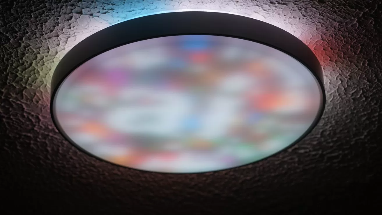 Round ceiling light with a frosted surface glowing softly, displaying blurred multicolored patterns, mounted on a textured dark ceiling with faint colored reflections around the edges
