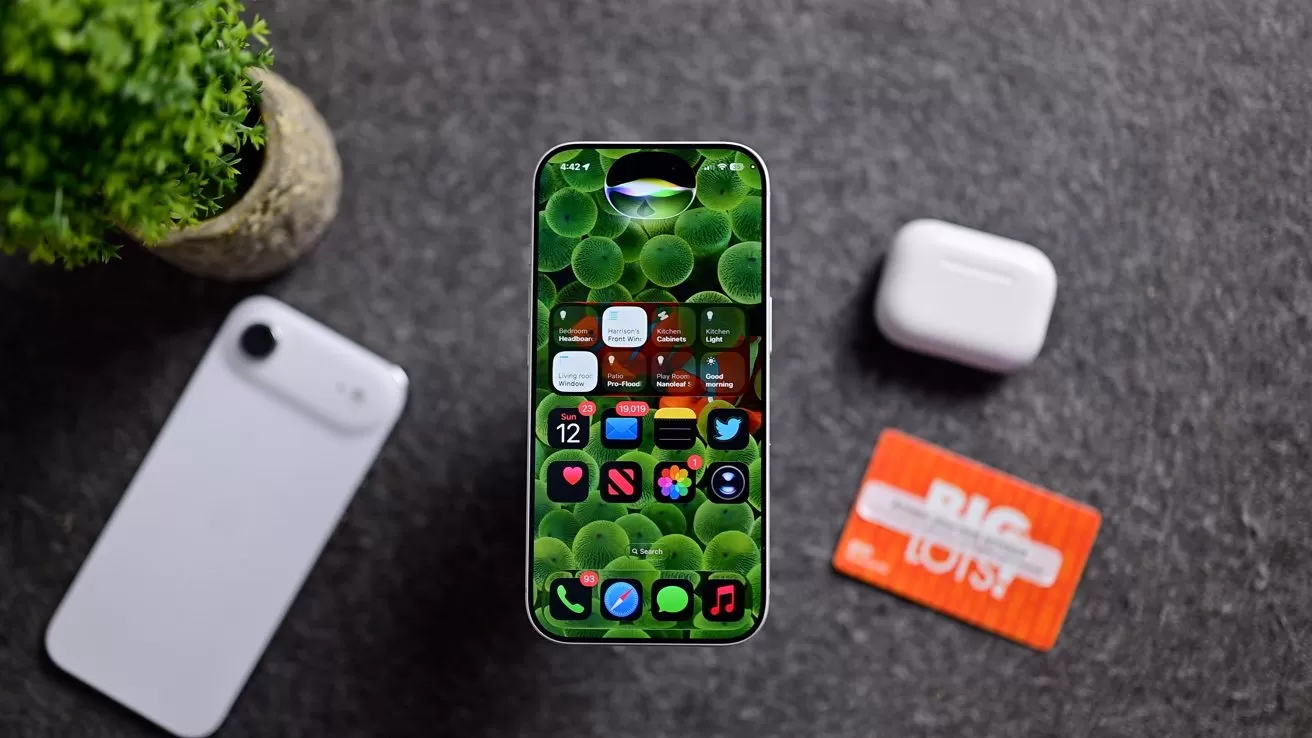Smartphone with colorful app-filled screen on gray surface, surrounded by a white phone, white wireless earbuds case, orange Big Lots gift card, and small green potted plant