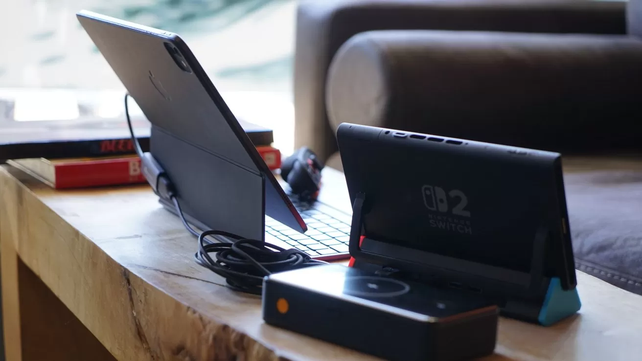 Tablet with keyboard, Nintendo Switch, and electronic device on a wooden table, surrounded by books and soft furnishings.